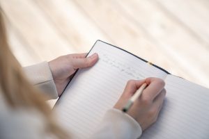 A person writing in a notebook with a pen, capturing a close-up view of hands.
